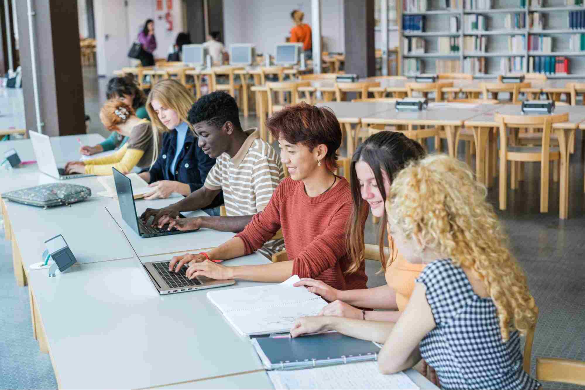 Students using laptops in a library, demonstrating how fiber supports growing communities with reliable internet for education and collaboration.