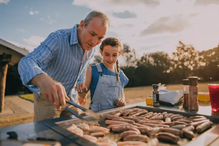 Father and daughter cooking together at an outdoor community barbecue.