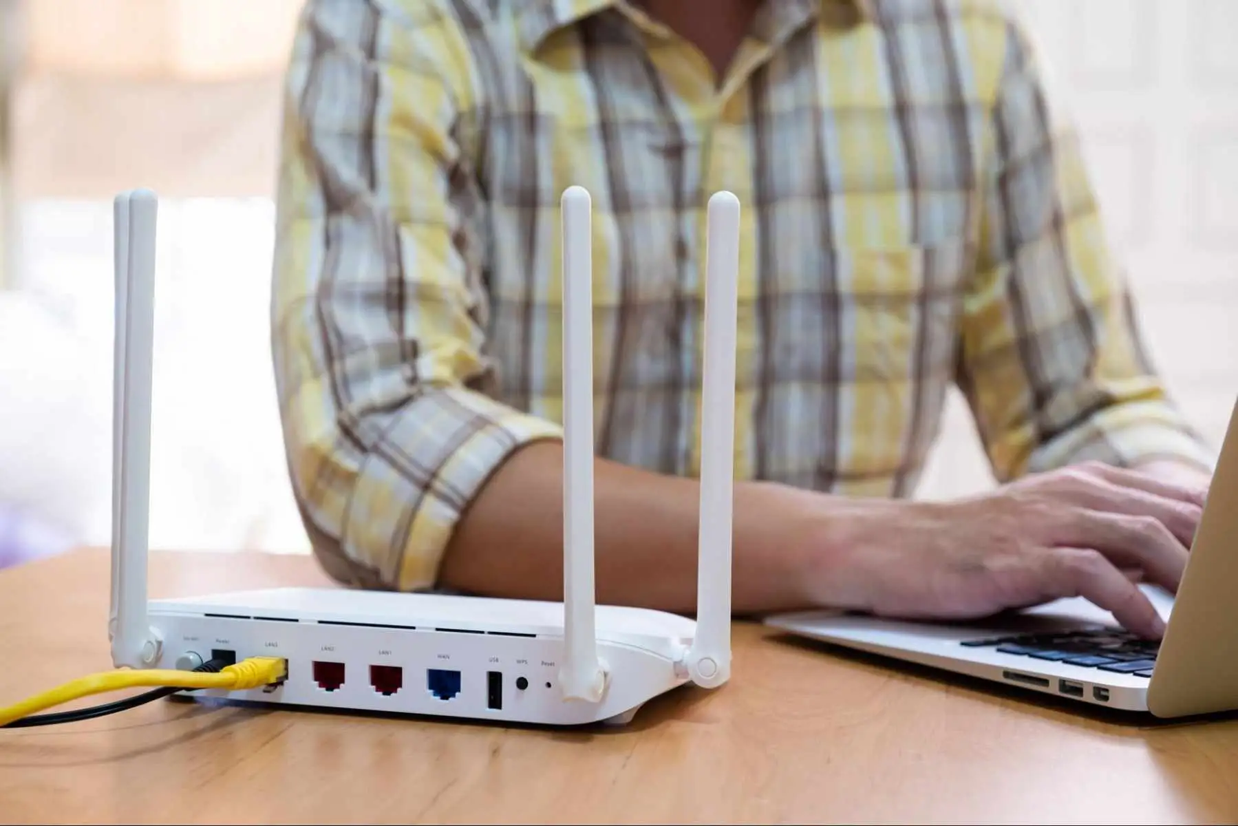 Person using a laptop beside a Wi-Fi router, representing the process of choosing an internet provider in Three Hills.
